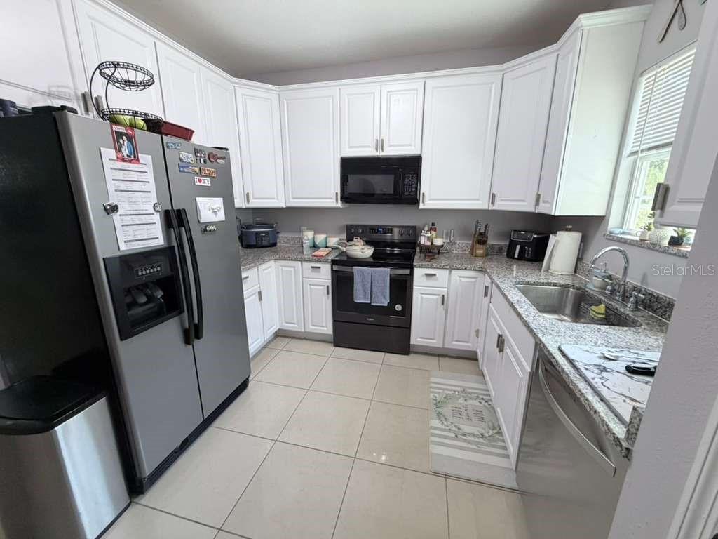 A kitchen features white cabinets, stainless steel appliances, granite countertops, and light-colored tile flooring — 1818 SUNNY STREET, KISSIMMEE, FL