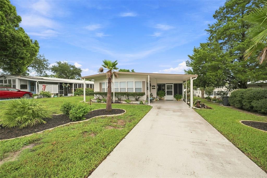 A single-story manufactured home with a concrete driveway, carport, and landscaped front yard — 8082 DELLROSE AVENUE, BROOKSVILLE, FL