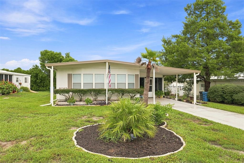 A single-story manufactured home features a front porch, a palm tree, and a concrete driveway — 8082 DELLROSE AVENUE, BROOKSVILLE, FL