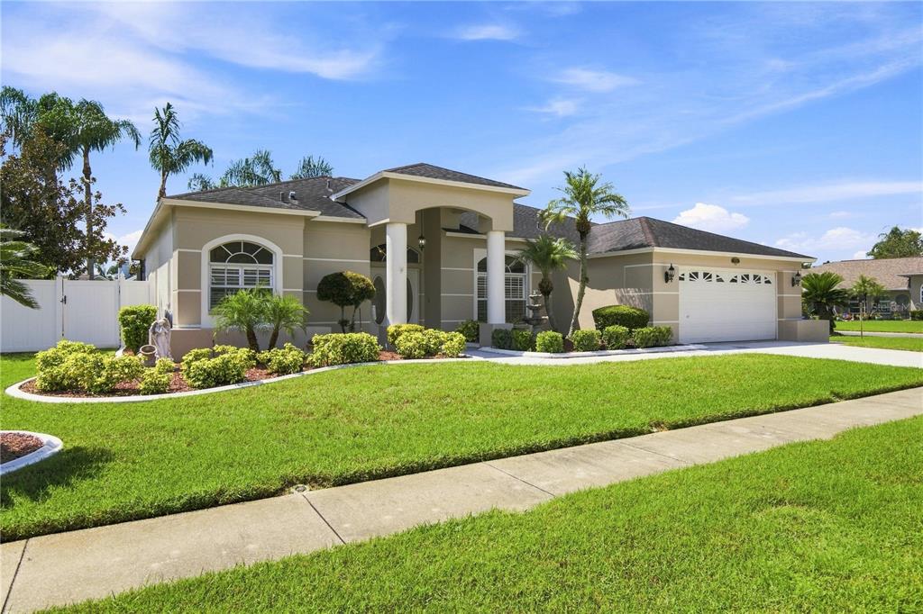 A single-story suburban house with a tan stucco exterior, a two-car garage, and landscaped lawn — 8704 CYPRESS LAKES BOULEVARD, NEW PORT RICHEY, FL