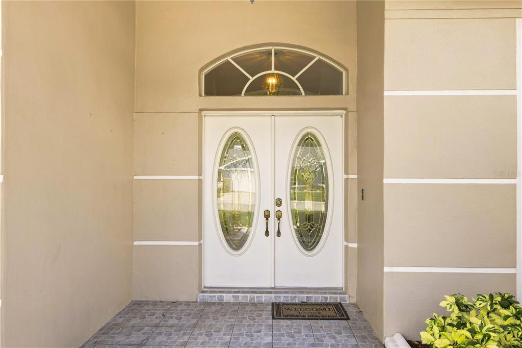 A double front door with oval glass inserts sits beneath a semi-circular transom window — 8704 CYPRESS LAKES BOULEVARD, NEW PORT RICHEY, FL