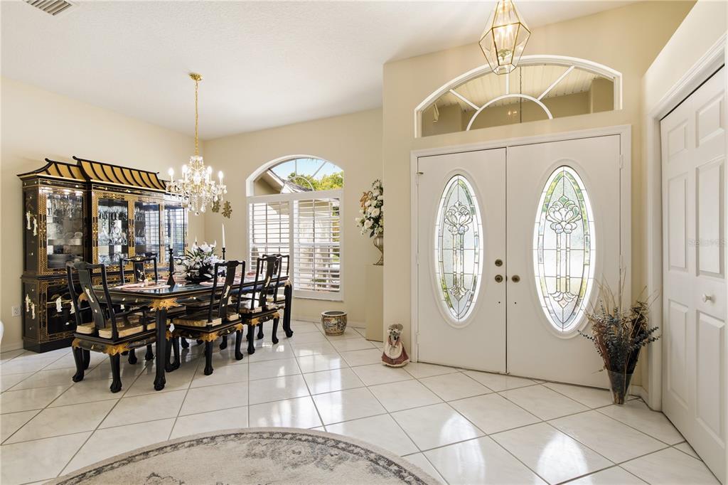 A dining area with a black lacquer furniture set and chandelier sits beside a white entryway — 8704 CYPRESS LAKES BOULEVARD, NEW PORT RICHEY, FL