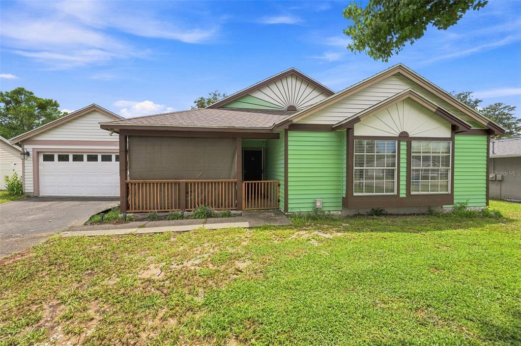 A green house with a front porch, attached garage, and a large grassy yard — 13094 LINDEN DRIVE, SPRING HILL, FL