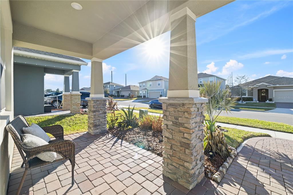 A covered front porch features stone-based columns, a brick paver floor, and a wicker chair — 2985 AMBERSWEET PLACE, CLERMONT, FL