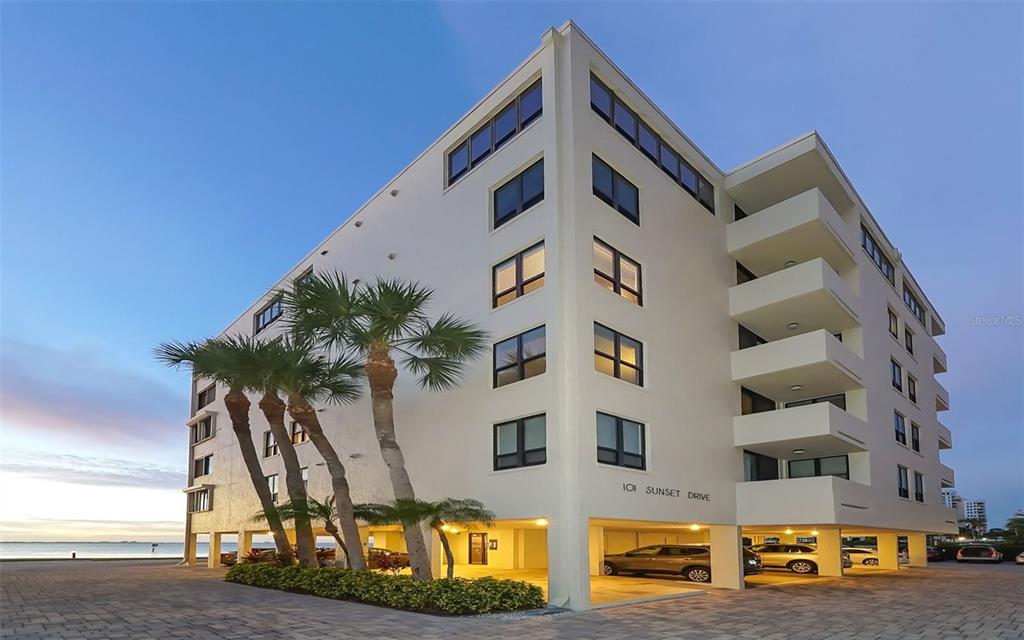A multi-story apartment building with a covered parking area and palm trees at sunset — 101 SUNSET DRIVE UNIT 103, SARASOTA, FL