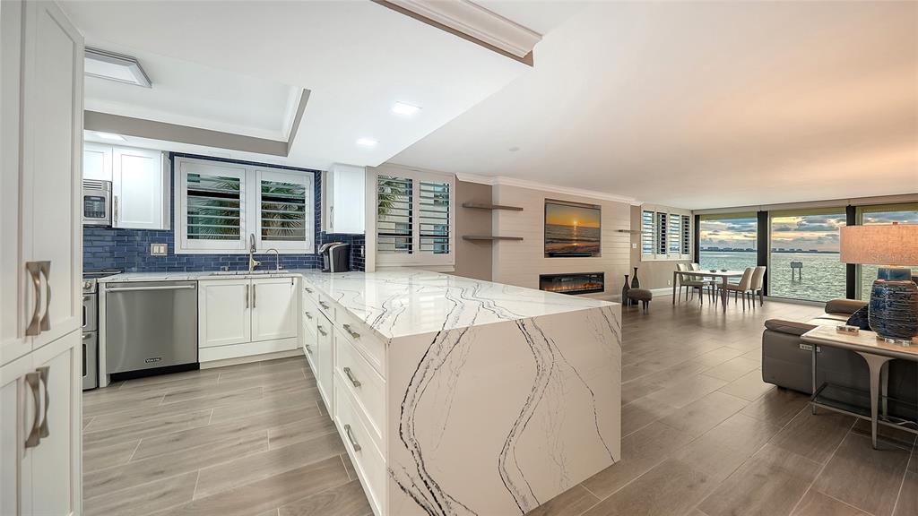 A modern kitchen with a waterfall island and white cabinets opens to a waterfront living area — 101 SUNSET DRIVE UNIT 103, SARASOTA, FL