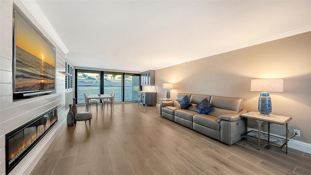 A living room with a fireplace, wall-mounted television, leather sofa, and floor-to-ceiling water views — 101 SUNSET DRIVE UNIT 103, SARASOTA, FL