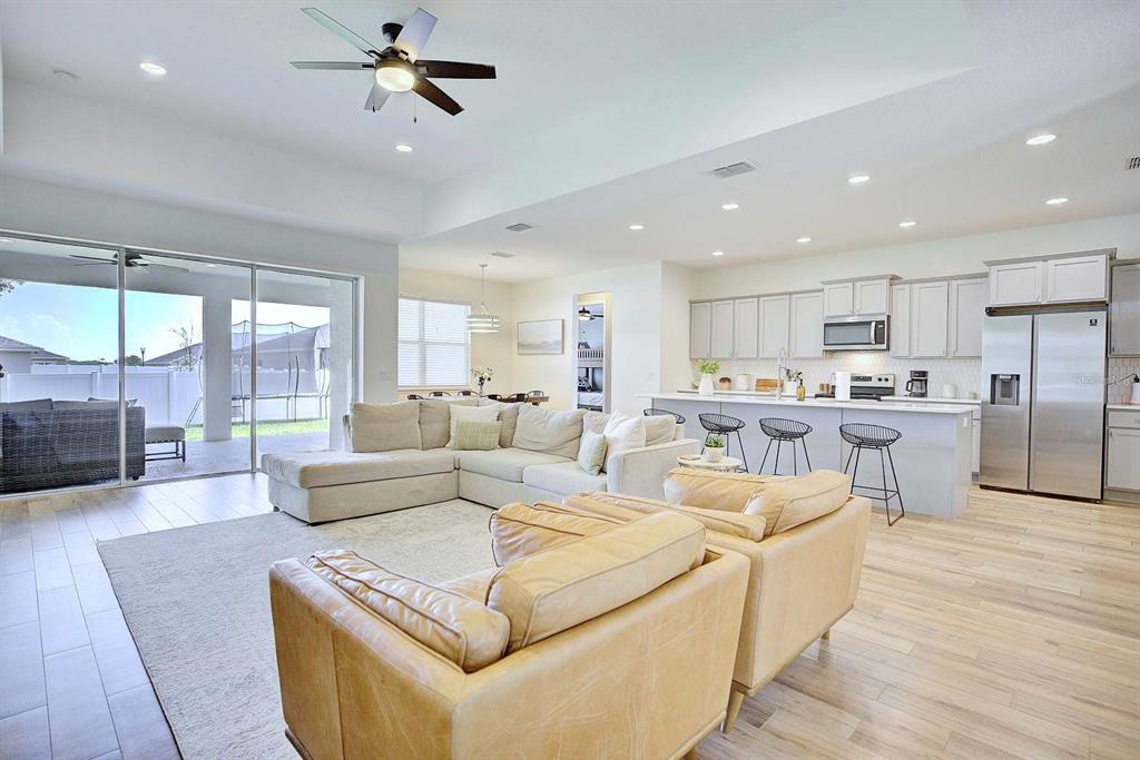 An open-concept living room and kitchen featuring light wood flooring, neutral furniture, and sliding doors — 1415 MAGNOLIA LANE, AUBURNDALE, FL