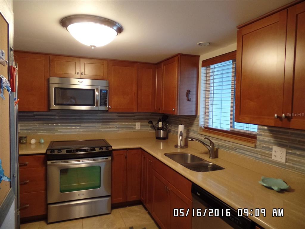 A kitchen features wood cabinets, stainless steel appliances, a tiled backsplash, and tan countertops — 815 OCEAN SHORE BOULEVARD UNIT 10A, ORMOND BEACH, FL