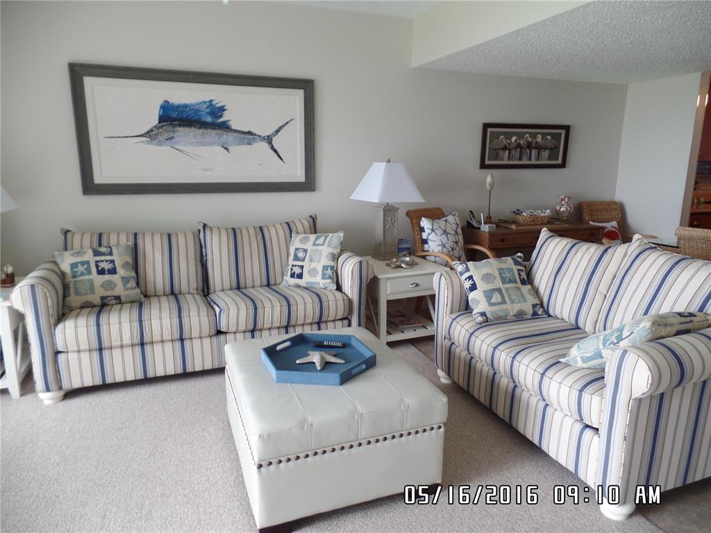 A living room features two striped sofas, a white ottoman, and coastal-themed wall art — 815 OCEAN SHORE BOULEVARD UNIT 10A, ORMOND BEACH, FL