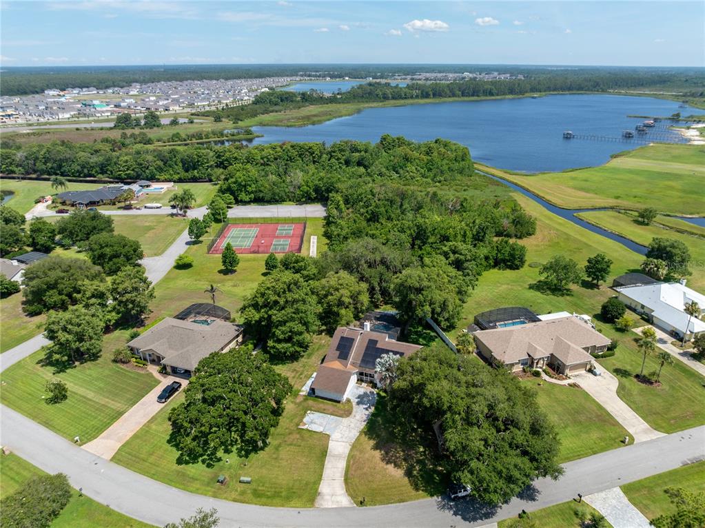 An aerial view shows three houses with pools, a tennis court, and a nearby lake — 3181 WHISPER WIND DRIVE, ST CLOUD, FL