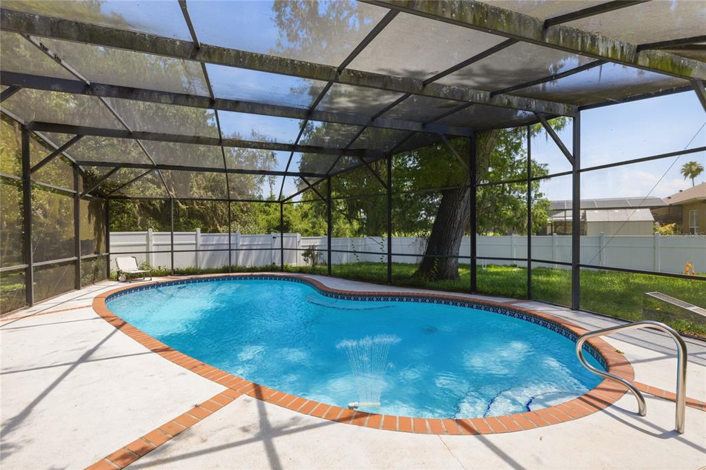 A screened-in swimming pool with a brick border sits on a concrete patio — 3181 WHISPER WIND DRIVE, ST CLOUD, FL