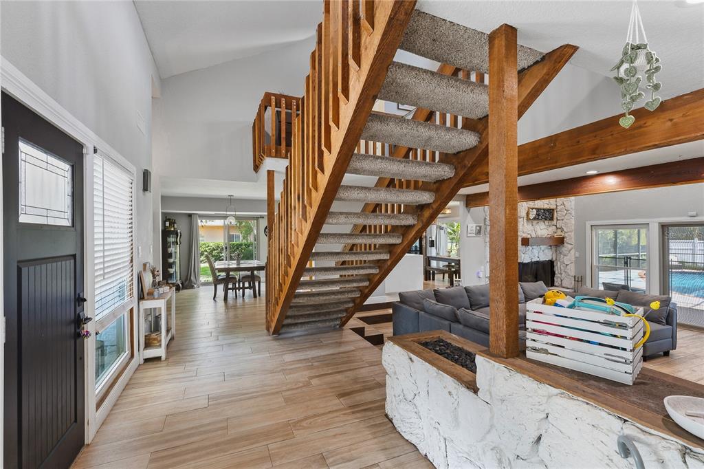 An open-concept living area features a wooden staircase, stone accents, and light wood-look flooring — 3181 WHISPER WIND DRIVE, ST CLOUD, FL