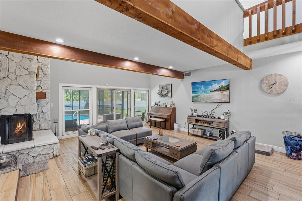 A living room features a stone fireplace, exposed wood beams, and a large sectional sofa — 3181 WHISPER WIND DRIVE, ST CLOUD, FL