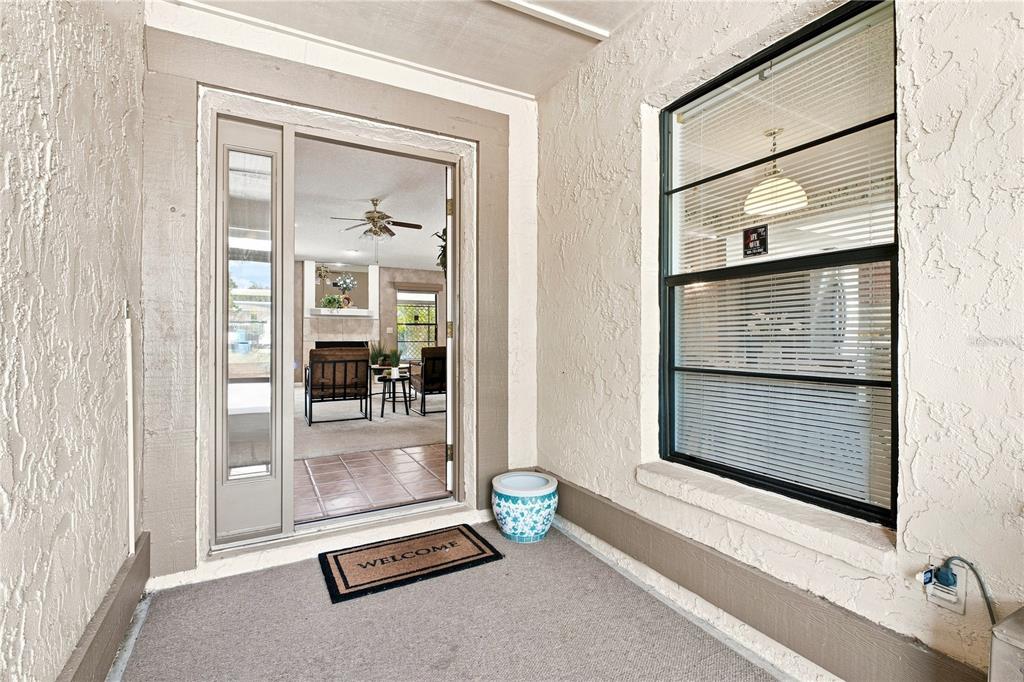 A covered entryway features a textured beige wall, a sliding glass door, and a welcome mat — 6803 LONGPOINTE WAY, TAMPA, FL