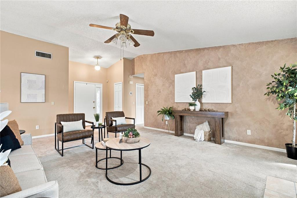 A living room features beige walls, a vaulted ceiling, a ceiling fan, and carpeted flooring — 6803 LONGPOINTE WAY, TAMPA, FL