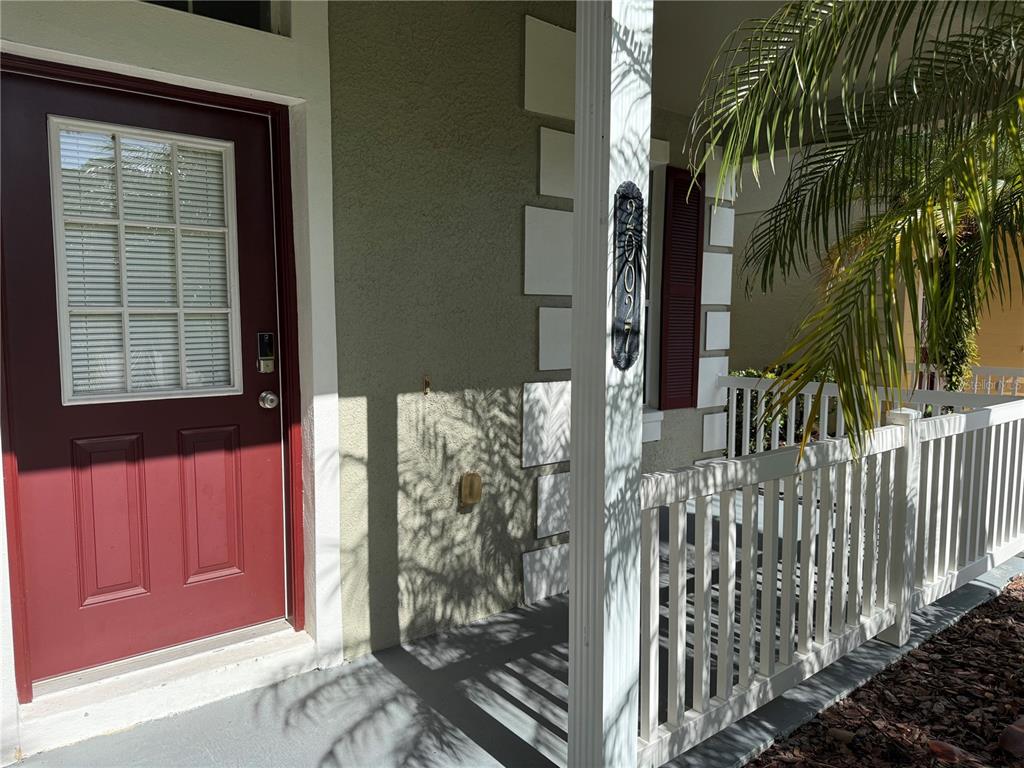 A red front door opens onto a covered porch with a white railing and palm tree — 20027 HERITAGE POINTE DRIVE, TAMPA, FL