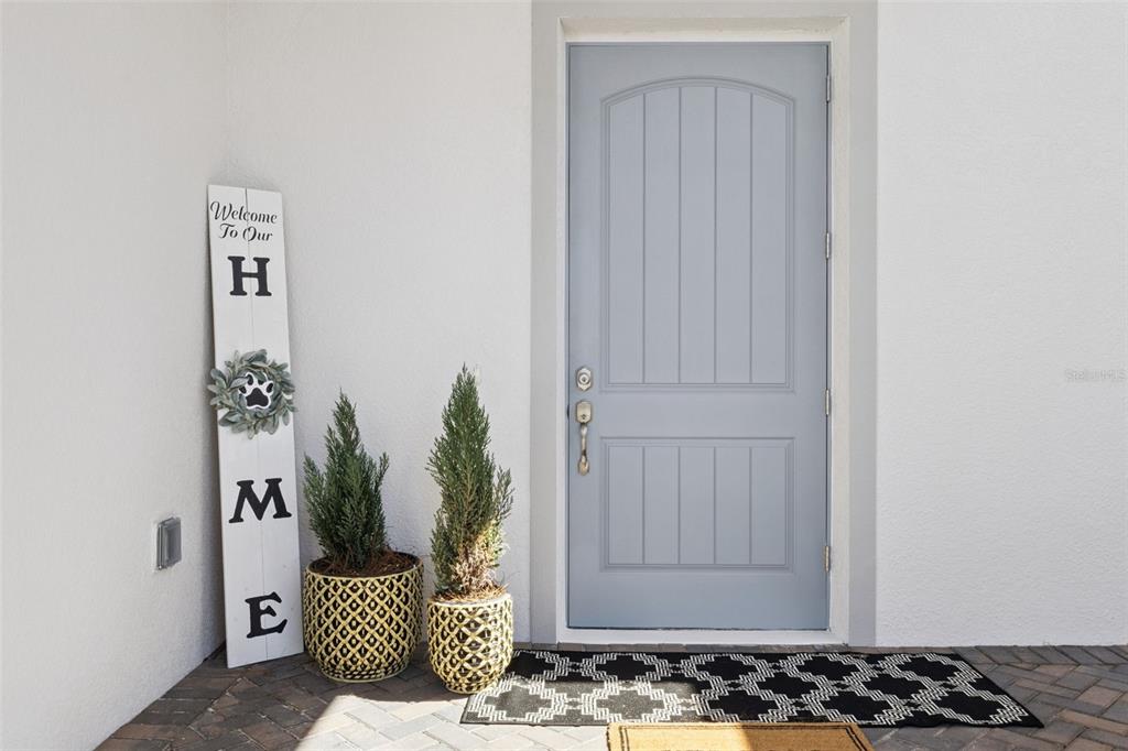 A light blue front door stands next to a vertical welcome sign and two potted plants — 4044 PINNACLE PLACE, LADY LAKE, FL