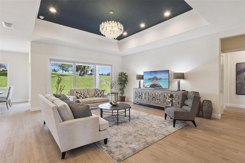 A living room features a tray ceiling, a chandelier, and a view of a grassy hill — 4044 PINNACLE PLACE, LADY LAKE, FL