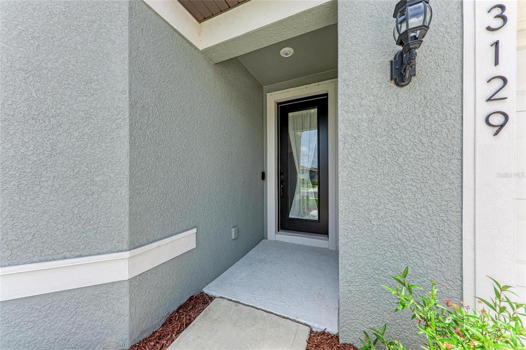 A gray stucco entryway features a dark front door with a glass insert and house numbers — 3129 61ST TERRACE E, ELLENTON, FL
