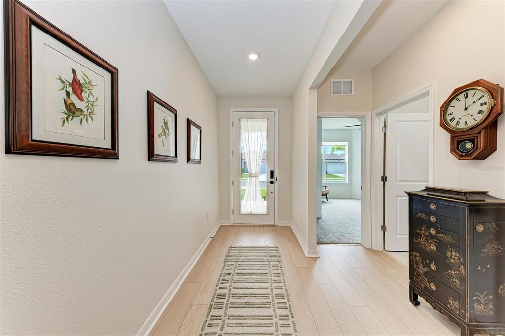 A bright entryway features light wood-look flooring, a runner rug, framed wall art, and a clock — 3129 61ST TERRACE E, ELLENTON, FL