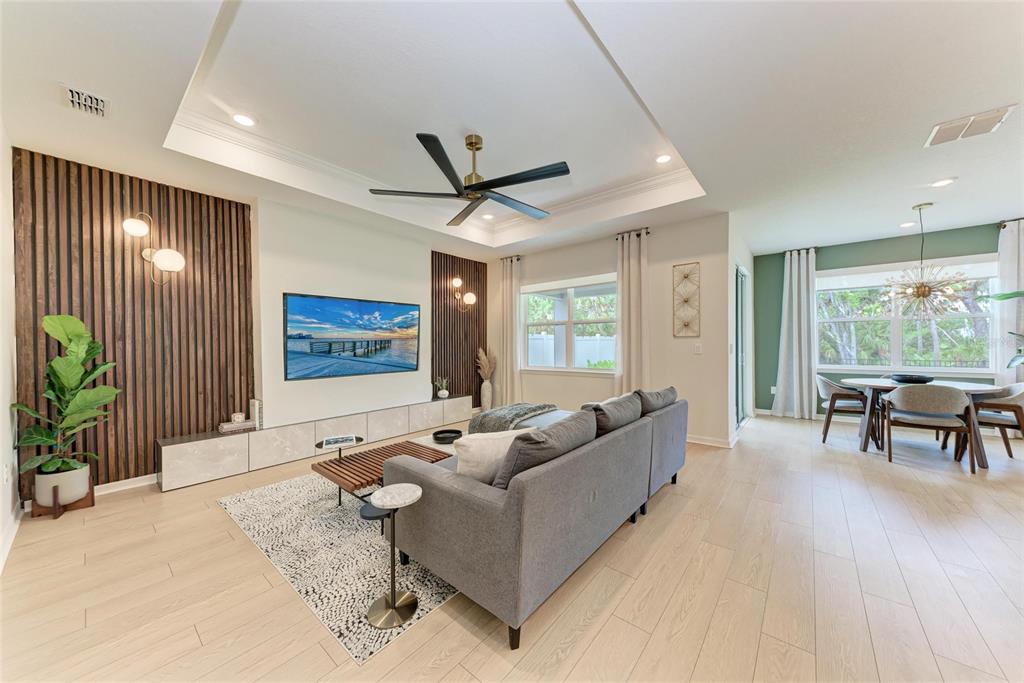 A modern living room features a slatted wood accent wall, a gray sectional, and dining area — 3129 61ST TERRACE E, ELLENTON, FL