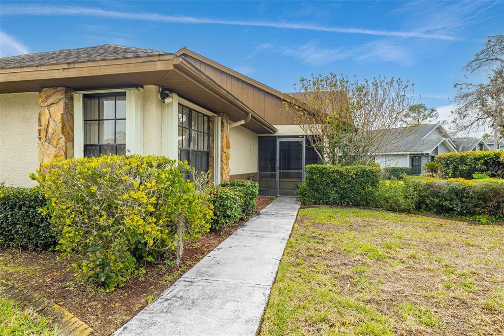 A concrete walkway leads to the screened front entryway of a single-story home — 7703 ROCKVILLE COURT, NEW PORT RICHEY, FL