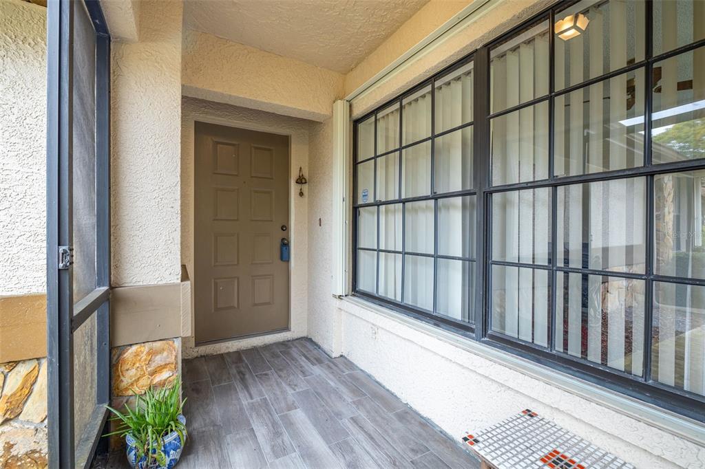 A covered entryway features a brown door, large grid windows, and grey wood-look tile flooring — 7703 ROCKVILLE COURT, NEW PORT RICHEY, FL
