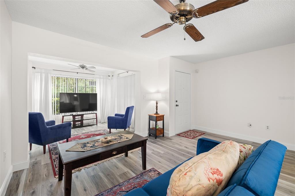 A living room features a blue sofa, two blue armchairs, a coffee table, and wood-look flooring — 7703 ROCKVILLE COURT, NEW PORT RICHEY, FL