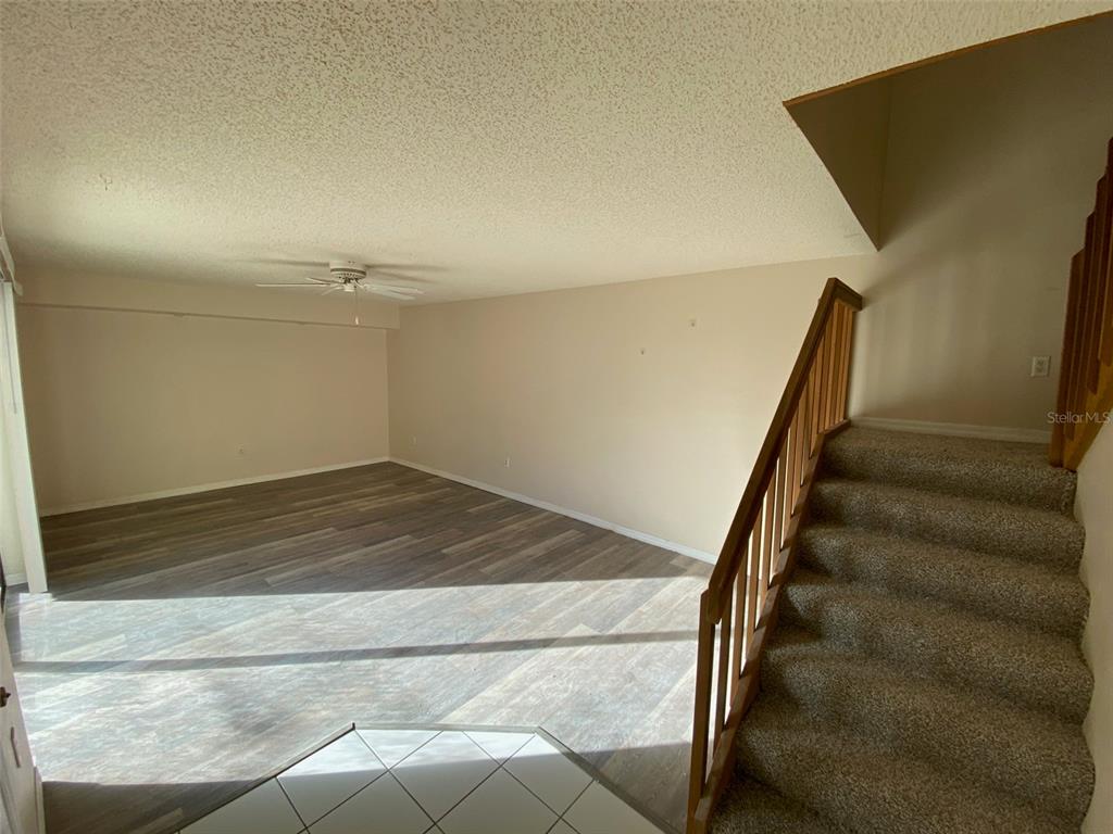 A living room features light-colored walls, wood-look flooring, a ceiling fan, and carpeted stairs — 2911 PECAN AVENUE, LEESBURG, FL