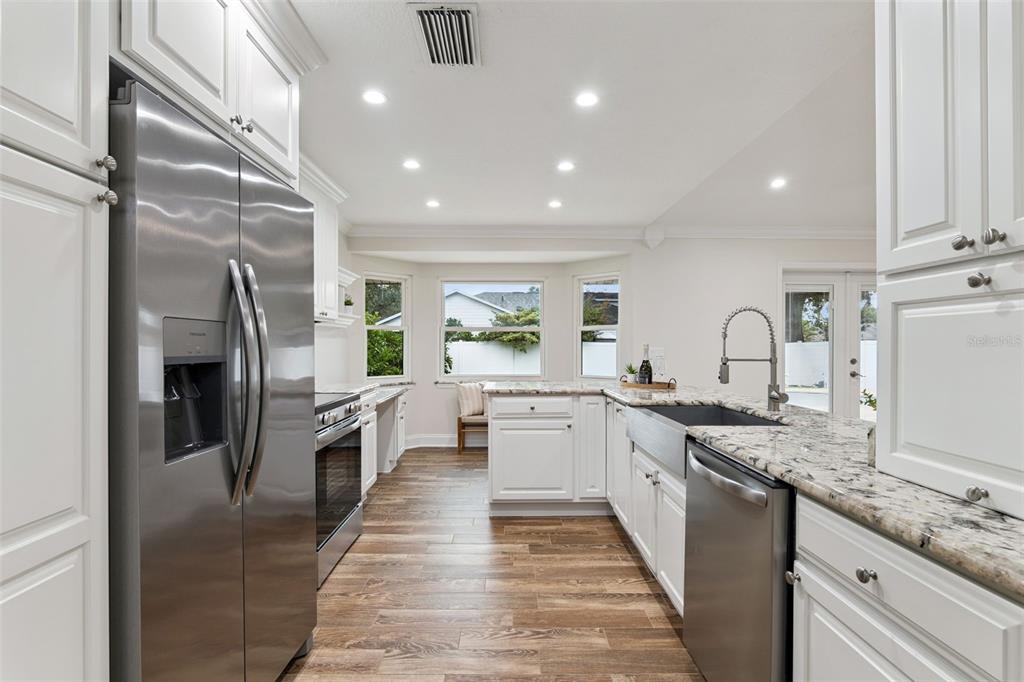 A white kitchen features stainless steel appliances, granite countertops, and wood-look flooring — 2450 DRESDEN TRAIL, APOPKA, FL