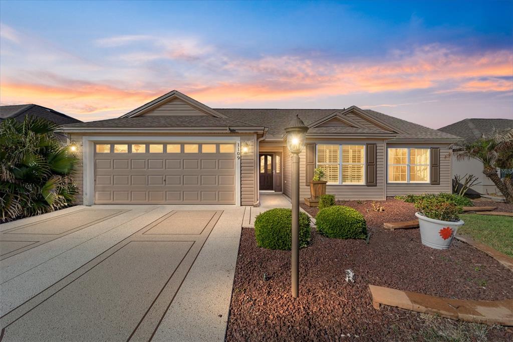 A single-story suburban house with a tan exterior, two-car garage, and a gravel front yard — 1109 ALCOVE LOOP, THE VILLAGES, FL