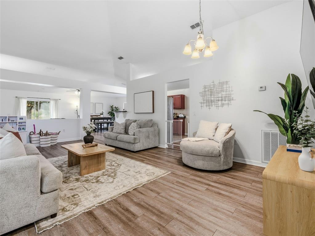 A bright living room features light wood-look flooring, neutral furniture, and a vaulted ceiling — 7357 CUMBRIA BOULEVARD, JACKSONVILLE, FL