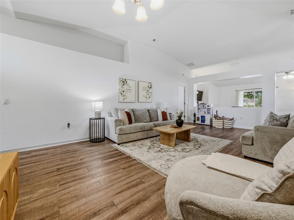 A living room features wood-look flooring, a gray sofa, a coffee table, and vaulted ceilings — 7357 CUMBRIA BOULEVARD, JACKSONVILLE, FL