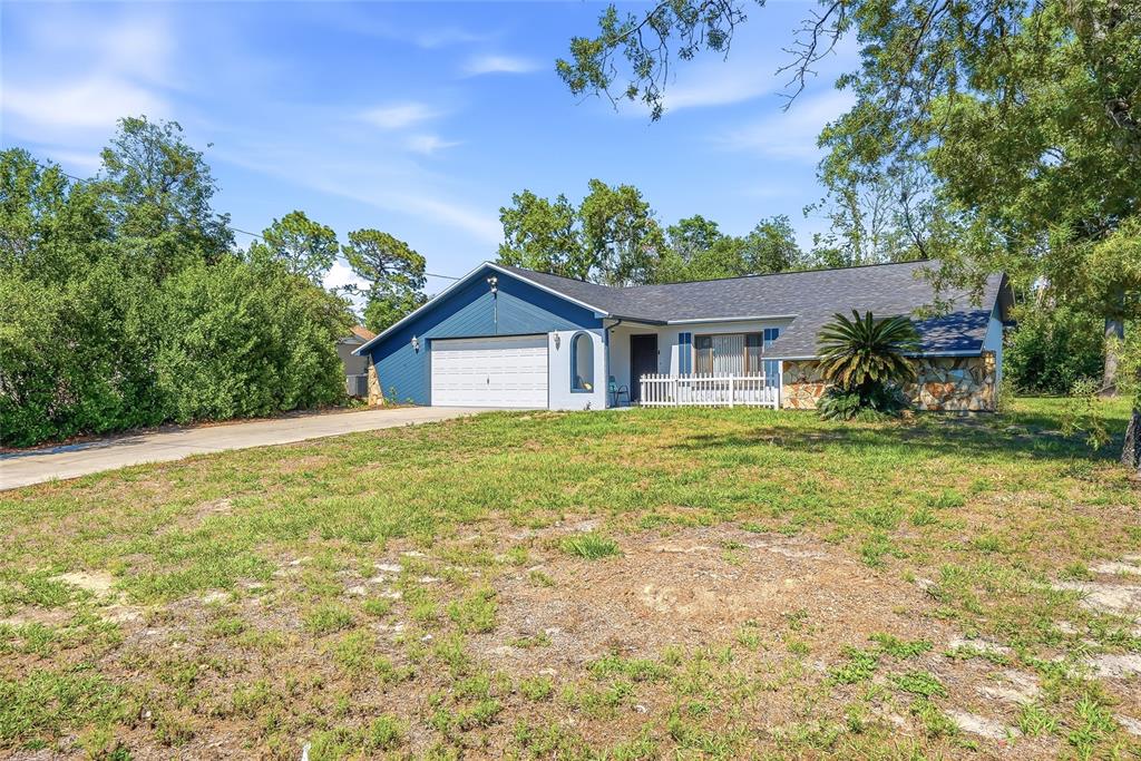 A single-story house with a blue garage, stone facade, and a white picket fence — 3276 MORVEN DRIVE, SPRING HILL, FL