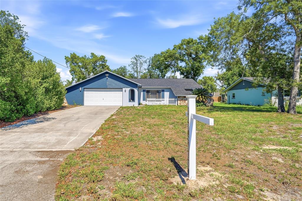 A single-story house with a blue garage and a white sign in the front yard — 3276 MORVEN DRIVE, SPRING HILL, FL