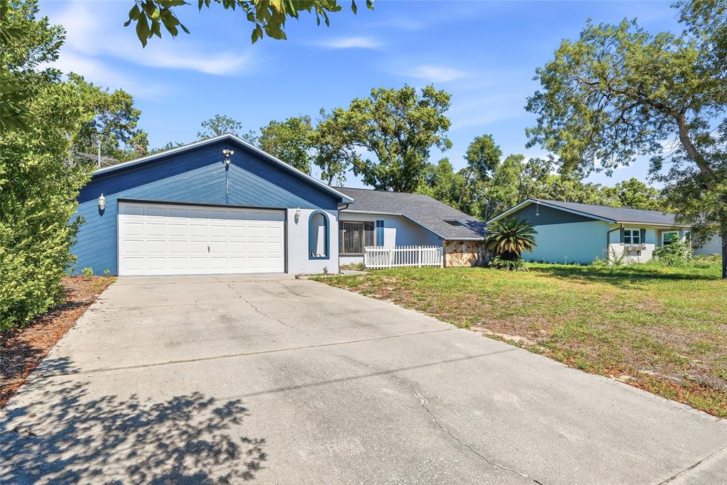 A blue house with a white garage door, concrete driveway, and a small white fence — 3276 MORVEN DRIVE, SPRING HILL, FL