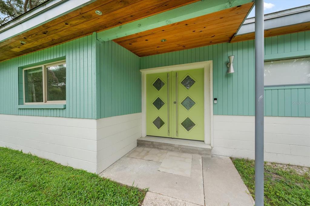 A mid-century modern home exterior features mint green vertical siding, a wood-paneled porch, and double doors — 533 BROXBURN AVENUE, TEMPLE TERRACE, FL