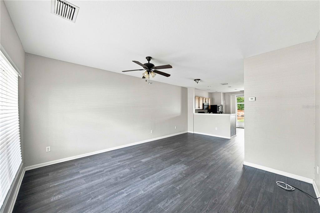A living room with gray wood-look flooring, a ceiling fan, and an open kitchen beyond — 4434 SW 49TH AVENUE, OCALA, FL