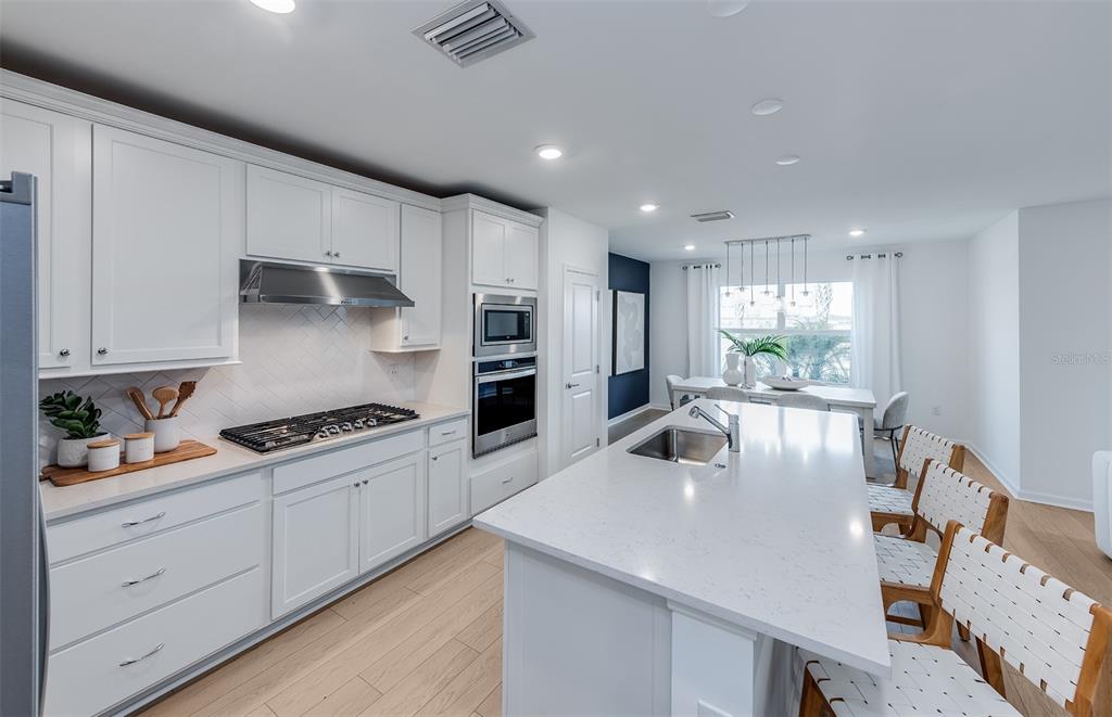 A modern white kitchen features a large quartz island, stainless steel appliances, and light wood flooring — 4809 FINLEY DRIVE, DAVENPORT, FL
