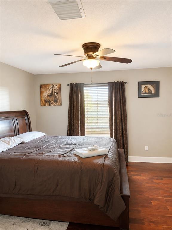 A bedroom features a wooden bed frame, dark curtains, a ceiling fan, and hardwood floors — 2927 CURVING OAKS WAY, ORLANDO, FL