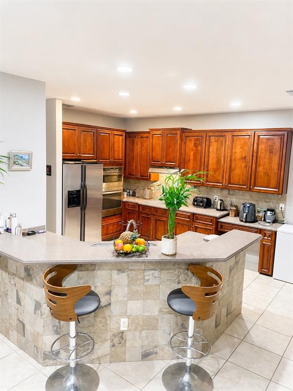 A kitchen features wood cabinets, stainless steel appliances, a tiled breakfast bar, and two stools — 2927 CURVING OAKS WAY, ORLANDO, FL