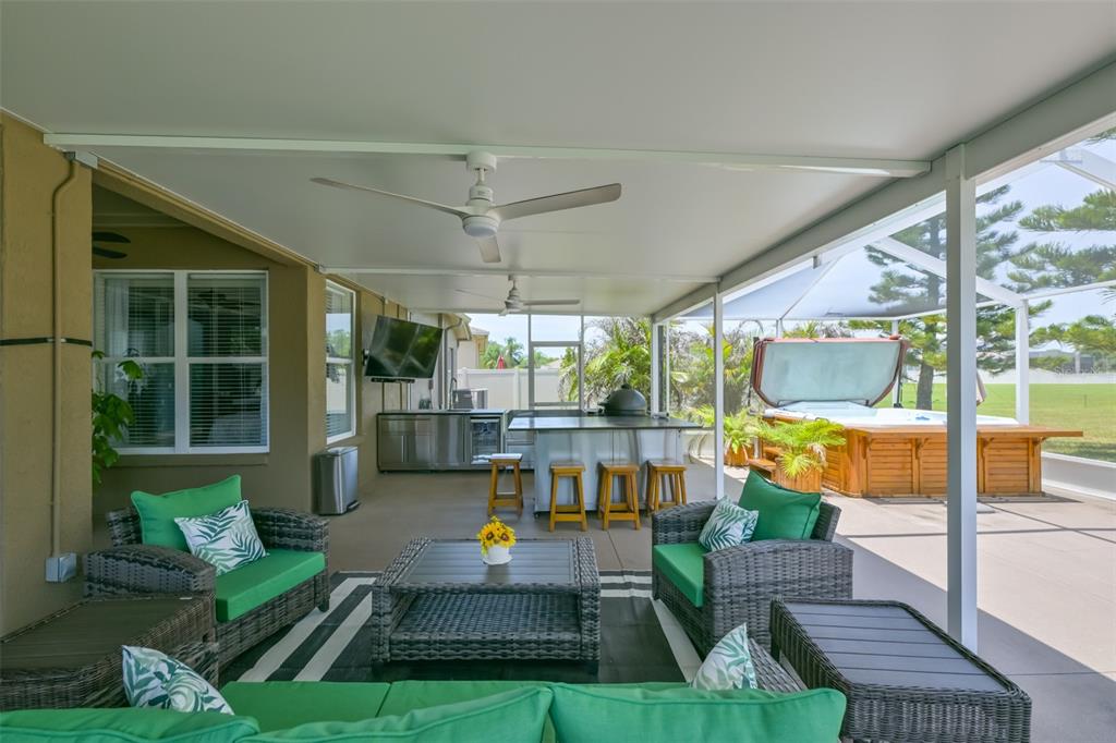 A covered patio features wicker furniture, a television, an outdoor kitchen, and a hot tub — 7318 GUILFORD PINE LANE, APOLLO BEACH, FL