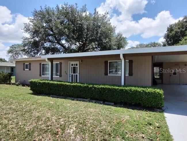 A single-story house with brown siding, a carport, and a manicured hedge in the front yard — 9180 SW 101ST PLACE, OCALA, FL