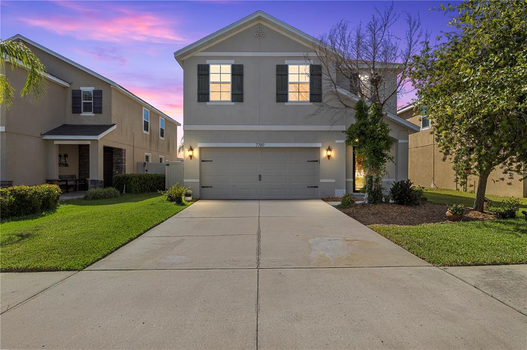 A two-story suburban house with a two-car garage and a concrete driveway at sunset — 7789 TUSCAN BAY CIRCLE, WESLEY CHAPEL, FL