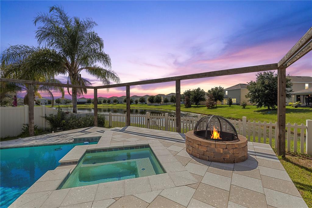 A backyard patio features a pool, a hot tub, and a stone fire pit at sunset — 7789 TUSCAN BAY CIRCLE, WESLEY CHAPEL, FL