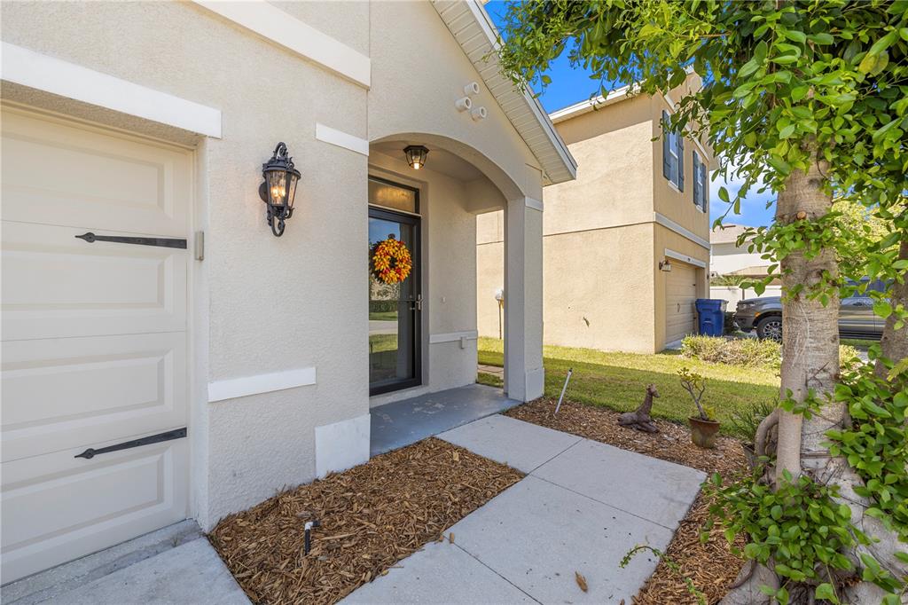 The exterior of a beige house features a front door, a garage, and a walkway — 7789 TUSCAN BAY CIRCLE, WESLEY CHAPEL, FL