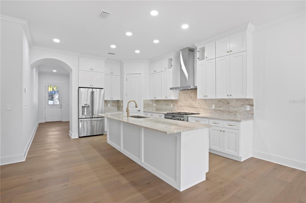 A modern white kitchen features a large island, stainless steel appliances, and light wood flooring — 4314 S RENELLIE DRIVE, TAMPA, FL