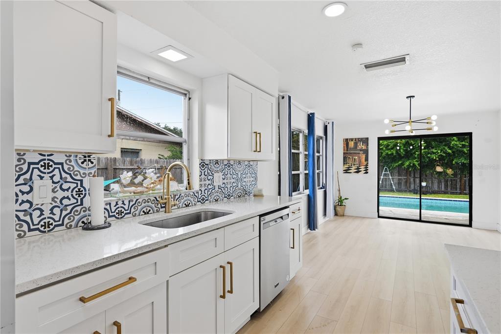 A kitchen with white cabinets, gold hardware, patterned tile backsplash, and a view of a pool — 835 MARLOWE AVENUE, ORLANDO, FL