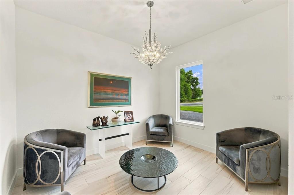 A sitting room features three gray velvet chairs, a glass console table, and a crystal chandelier — 1113 HOLSTONS POINTE PLACE, GOTHA, FL